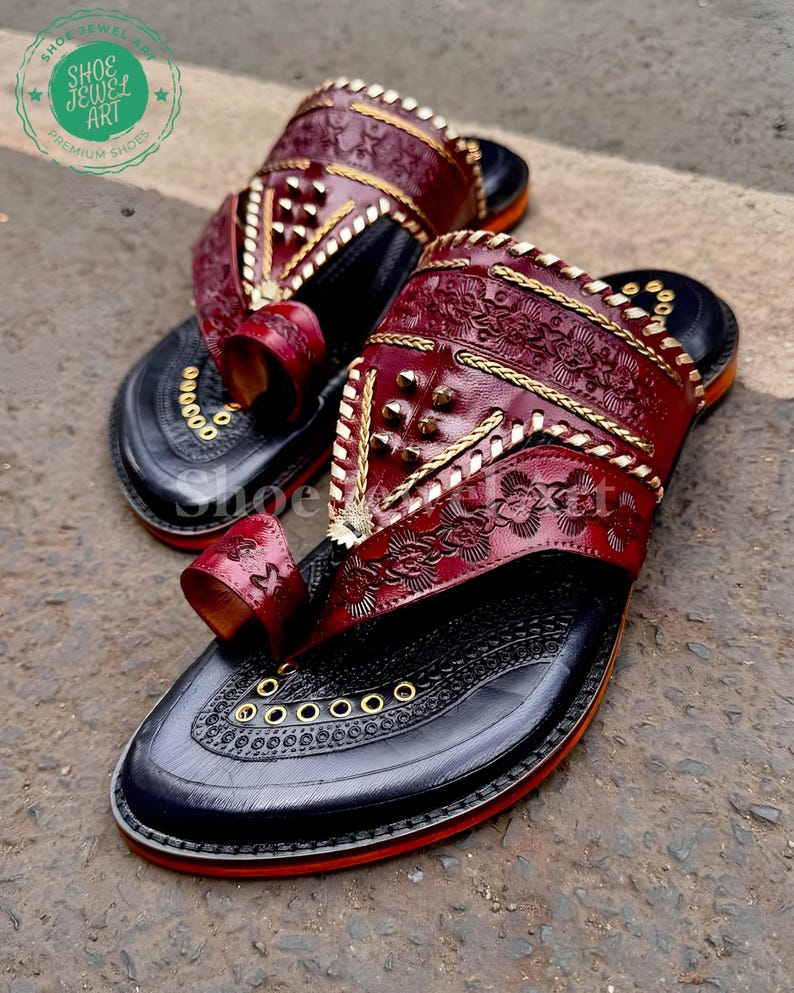 Puede incluir: Un par de sandalias de cuero hechas a mano. Las sandalias presentan una parte superior de cuero rojo oscuro con intrincados patrones florales en relieve y costuras doradas. Las suelas son negras con ribete rojo y ojales dorados. C&oacute;modas y elegantes.
