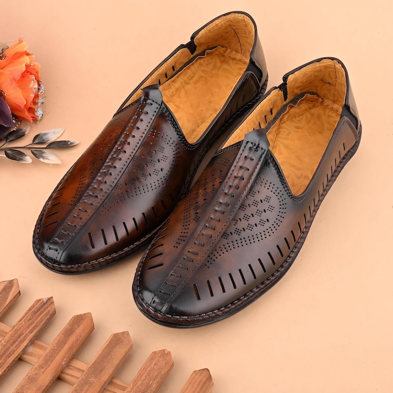 May include: A pair of brown leather slip-on shoes with decorative perforations and stitching. The shoes have a rounded toe and a light brown interior. The leather has a polished finish, and the shoes are set against a neutral background.