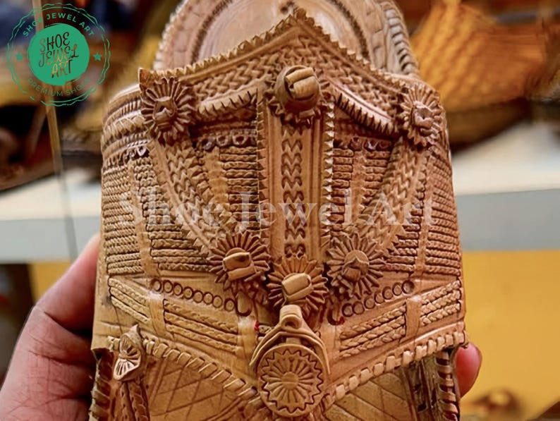 May include: Close-up of a carved wooden object with intricate floral and geometric patterns. The object is a light brown color and features detailed relief work, including circular and star-like designs. The image is well-lit, highlighting the texture and craftsmanship.