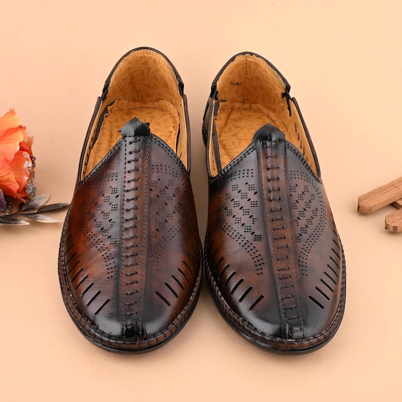 May include: A pair of brown leather slip-on shoes with intricate cut-out designs and a black trim. The shoes have a pointed toe and a stitched center seam. The interior is a light tan color.