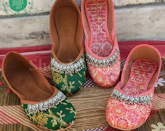 Op de afbeelding: Vier paar versierde platte schoenen. Twee paar hebben een groen geborduurd ontwerp met zilverkleurige kralen, en de andere twee paar hebben een roze en oranje bloemenpatroon met zilverkleurige kralen. De schoenen hebben bruine leren zolen.