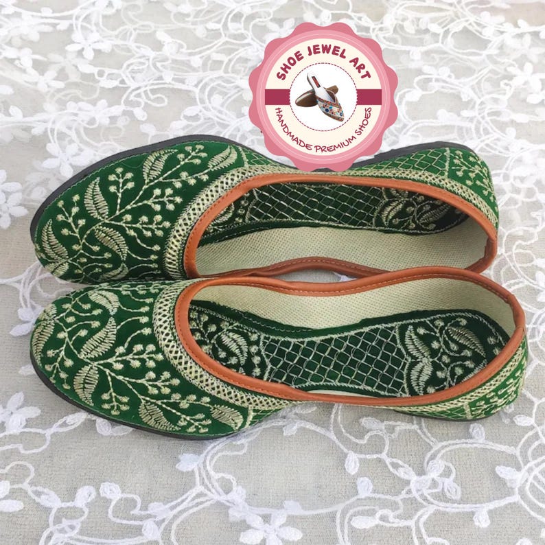 K&ouml;nnte beinhalten: Ein Paar gr&uuml;ne, bestickte Slipper mit floralem Design. Die Schuhe haben eine beige Einfassung und eine dunkelgr&uuml;ne Sohle. Das pinkfarbene kreisf&ouml;rmige Logo zeigt "Shoe Jewel Art, Handmade Premium Shoes".