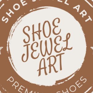 May include: A brown and white circular logo with the text "SHOE JEWEL ART" in a decorative font. The words are arranged in a circle, with "SHOE JEWEL ART" in the center. Two stars are on either side of the center text.