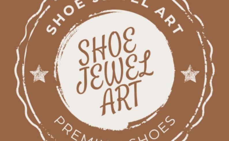 May include: A brown and white circular logo with the text "SHOE JEWEL ART" in a decorative font. The words are arranged in a circle, with "SHOE JEWEL ART" in the center. Two stars are on either side of the center text.