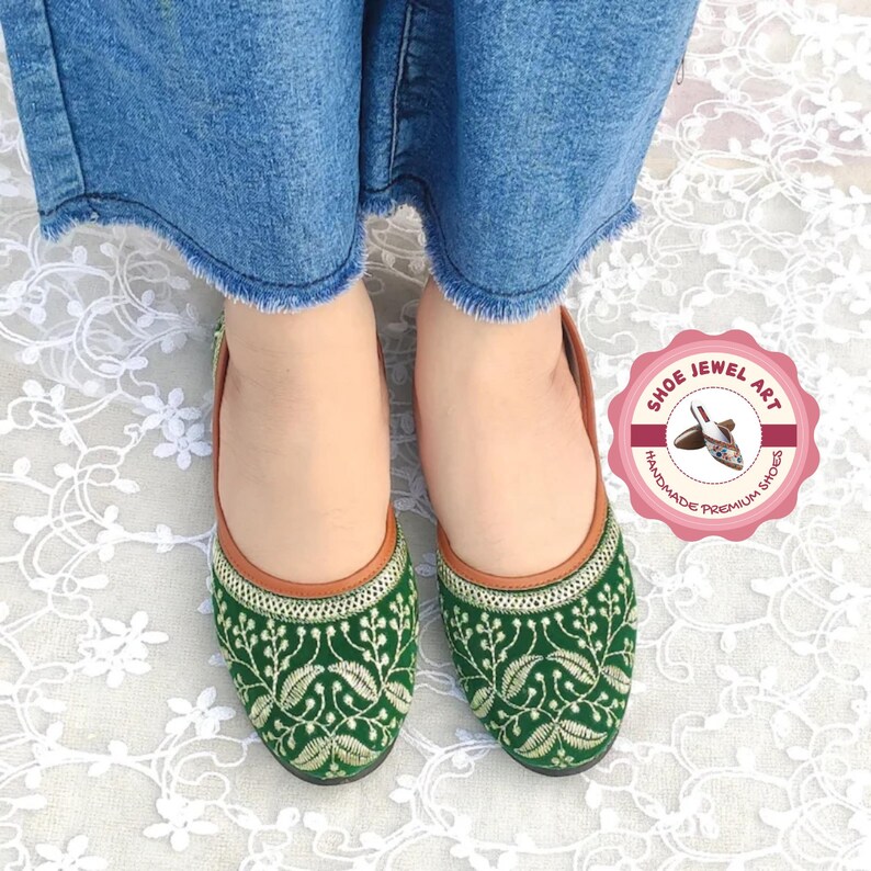 K&ouml;nnte beinhalten: Gr&uuml;ne, bestickte Ballerinas mit floralem Design und braunem Besatz. Die Schuhe sind handgefertigt und tragen den Text "Shoe Jewel Art" auf einem rosa kreisf&ouml;rmigen Logo. Die Schuhe werden mit blauen Jeans getragen.