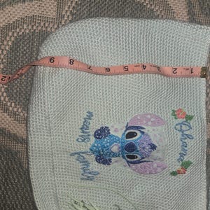 Puede incluir: Bolso blanco de crochet con un personaje de Stitch bordado en azul y morado, de la pel&iacute;cula de Disney Lilo & Stitch. El bordado incluye el texto "Ohana means family".
