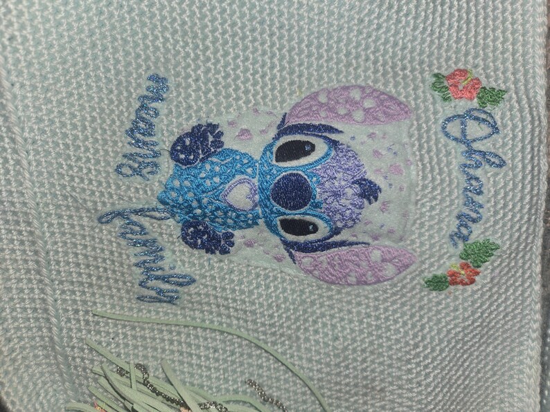 Puede incluir: Un dise&ntilde;o bordado en azul claro y morado de un personaje de Stitch de la pel&iacute;cula de Disney Lilo & Stitch. El dise&ntilde;o est&aacute; en una tela blanca con las palabras "My Family Always" y "Ohana" bordadas en azul.