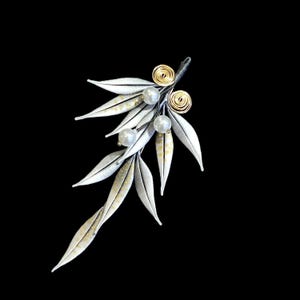 Puede incluir: Broche plateado con forma de rama de olivo estilizada. El broche presenta delicadas hojas con detalles dorados, perlas de imitación y detalles de alambre de oro enrollado. El diseño está sobre un fondo negro.
