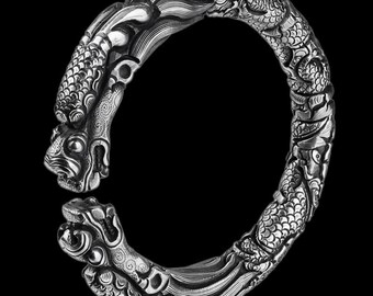 May include: A silver-colored bracelet with a dragon design. The bracelet features detailed carvings of a dragon's head and body, with scales and flowing lines. The bracelet is set against a black background.