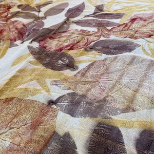 May include: A white fabric with brown, red, and yellow leaf prints. The fabric has a textured surface and a subtle sheen.