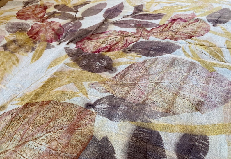 May include: A white fabric with brown, red, and yellow leaf prints. The fabric has a textured surface and a subtle sheen.