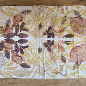 May include: A white fabric with a symmetrical pattern of brown, yellow, and red leaf prints. The fabric has a natural, organic feel.