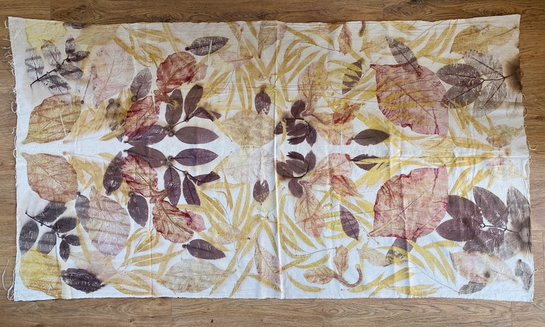 May include: A white fabric with a symmetrical pattern of brown, yellow, and red leaf prints. The fabric has a natural, organic feel.