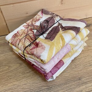 May include: A stack of four fabric napkins with a leaf print in shades of brown, yellow, and pink. The napkins are tied together with a black ribbon.