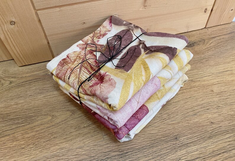 May include: A stack of four fabric napkins with a leaf print in shades of brown, yellow, and pink. The napkins are tied together with a black ribbon.