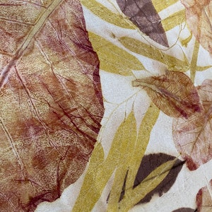 May include: A close-up of a fabric with a leaf pattern. The leaves are in shades of brown, red, and yellow. The fabric has a white background.