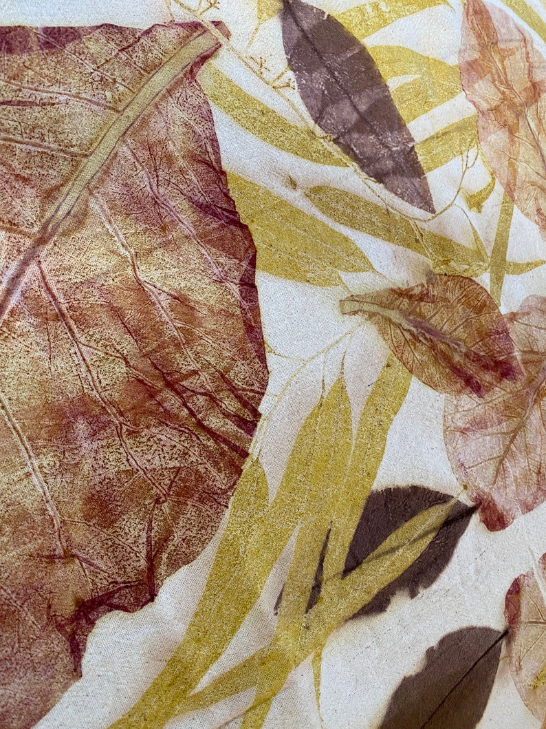 May include: A close-up of a fabric with a leaf pattern. The leaves are in shades of brown, red, and yellow. The fabric has a white background.