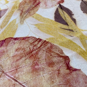 May include: Close-up of a leaf print on fabric. The leaf is a deep red-brown colour with a yellow-gold outline. The fabric is a light cream colour.