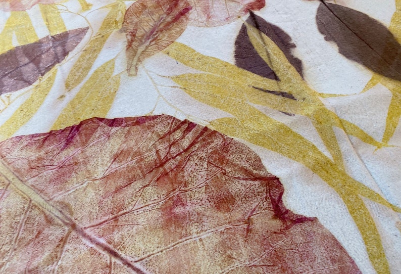 May include: Close-up of a leaf print on fabric. The leaf is a deep red-brown colour with a yellow-gold outline. The fabric is a light cream colour.