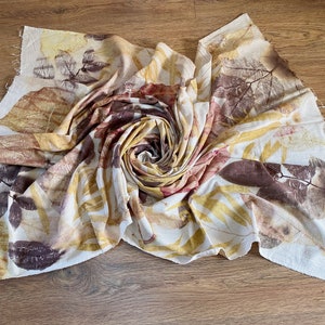 May include: A white fabric with brown, yellow and red leaf prints. The fabric is folded into a spiral shape.