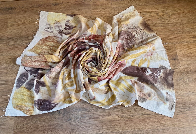 May include: A white fabric with brown, yellow and red leaf prints. The fabric is folded into a spiral shape.