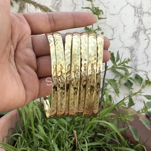 May include: A set of eight gold-toned hammered metal bangles. The bangles are stacked on top of each other and are all the same width.