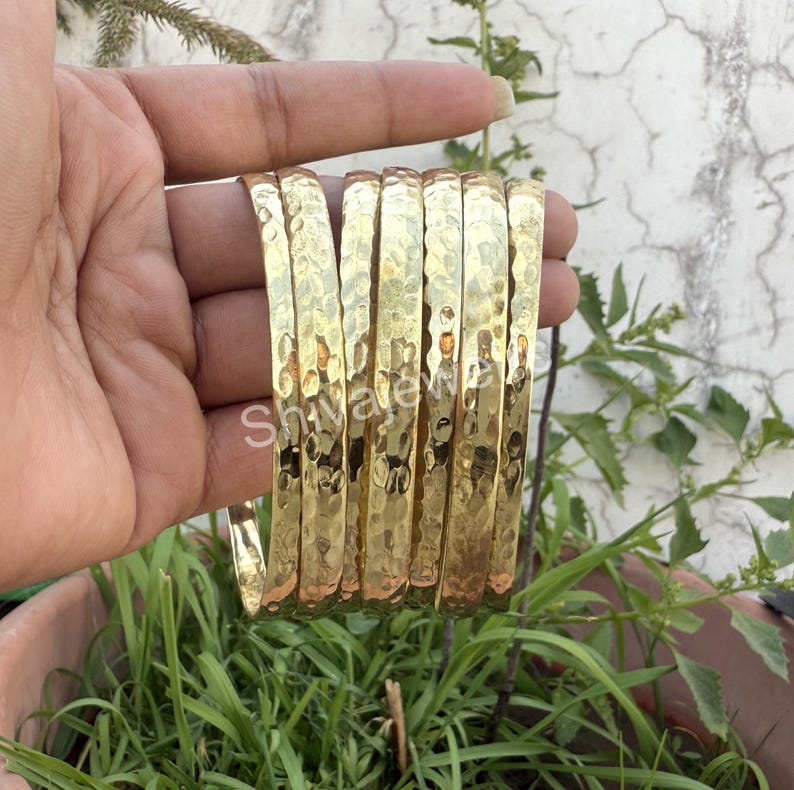 May include: A set of eight gold-toned hammered metal bangles. The bangles are stacked on top of each other and are all the same width.