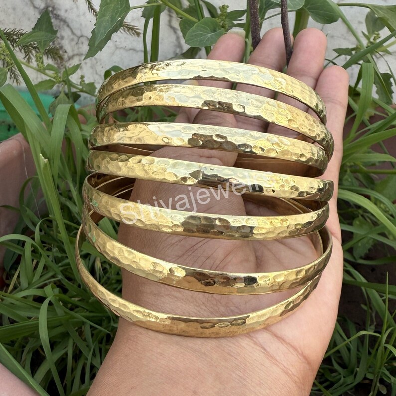 May include: A set of six gold-toned hammered metal bangles. The bangles are stacked on top of each other and are slightly curved.