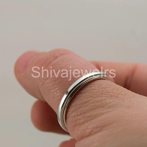 Puede incluir: Primer plano de un anillo de plata en un dedo. El anillo es delgado y tiene un diseño simple y elegante. El texto "Shivajewels" es visible en la imagen.