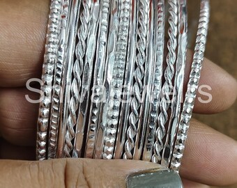 May include: A stack of silver bangles with different textured designs. The bangles are stacked on top of each other and are all the same width.
