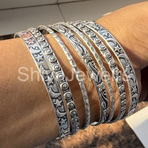 May include: A set of silver bangles featuring moon and star designs. The bangles are stacked on a person's wrist.