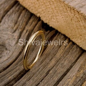 May include: A gold ring featuring a double band design. The ring is displayed on a rustic wooden surface, with the text "Shwajewelrs" visible. The ring's polished surface reflects light, showcasing its elegant simplicity.