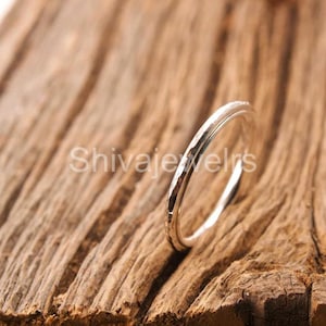 May include: A silver ring with a hammered texture, set against a backdrop of aged wood. The ring's design is simple and elegant. The word "ShivajeJewels" is visible in the background.