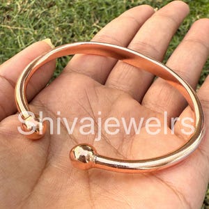 Puede incluir: Un brazalete de cobre con extremos redondeados. El brazalete es simple y minimalista.
