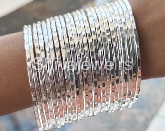 May include: A stack of silver hammered bangle bracelets. The bracelets are stacked on a person's wrist.