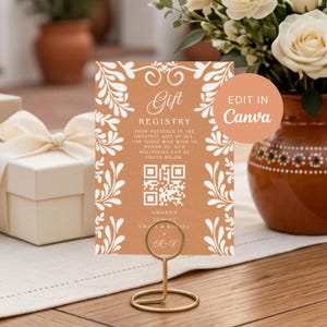 Könnte beinhalten: Ein rechteckiges Geschenkelistenschild in Terrakotta-Orange mit weißen botanischen Rändern und einem zentralen QR-Code. Der Text lautet Gift Registry, Your presence is the greatest gift of all, Amazon, Target und die Namen Craig & Rachel mit A-V.