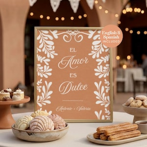 May include: A rectangular sign in a gold frame with a terracotta background and white floral borders. The text reads EL Amor ES Dulce and Antonio + Valeria. A circular sticker in the top right corner states English & Spanish INCLUDED.