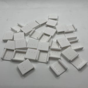 May include: A pile of white plastic earring backs. The backs have four small holes in them.