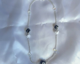 May include: A silver chain necklace with black and white dice charms and a black 8-ball charm.