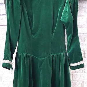 May include: A green velvet dress with a white lace trim around the neckline and sleeves. The dress has a fitted bodice and a full skirt.