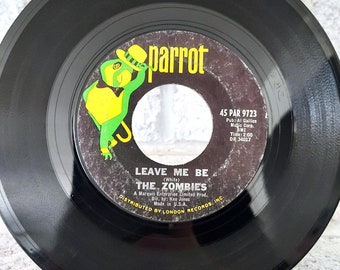 May include: Black vinyl record with a green parrot logo and the text "parrot" in white. The record is labeled with the song title "Leave Me Be" by "The Zombies" and the record label information "45 PAR 9723".