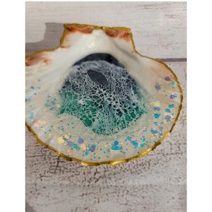 May include: A seashell dish with a green, blue, and white resin inlay. The resin has a glittery finish and is surrounded by a gold rim.