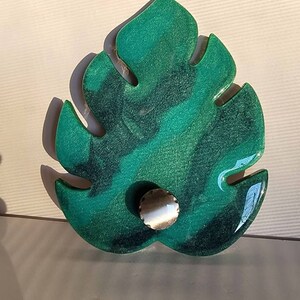 May include: A green and blue resin leaf with a silver knob in the center. The leaf is shaped like a monstera leaf.