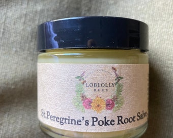 May include: A small glass jar with a black lid, filled with a light yellow salve. The label reads "Loblolly Bees" and "St. Peregrine's Poke Root Salve" with floral illustrations. The jar sits on a green fabric surface.