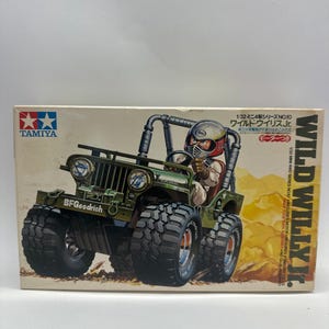 May include: A model kit box featuring a green Wild Willy Jr. jeep with large tires and a driver figure. The box has the Tamiya logo and text in Japanese and English, including "BFGoodrich".