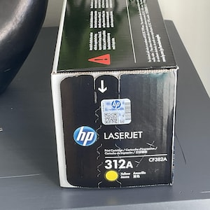May include: A black and yellow HP LaserJet 312A print cartridge box. The box features the HP logo, product information, and a yellow circle indicating the color. The box also includes the text "Print Cartridge" and "CF382A".