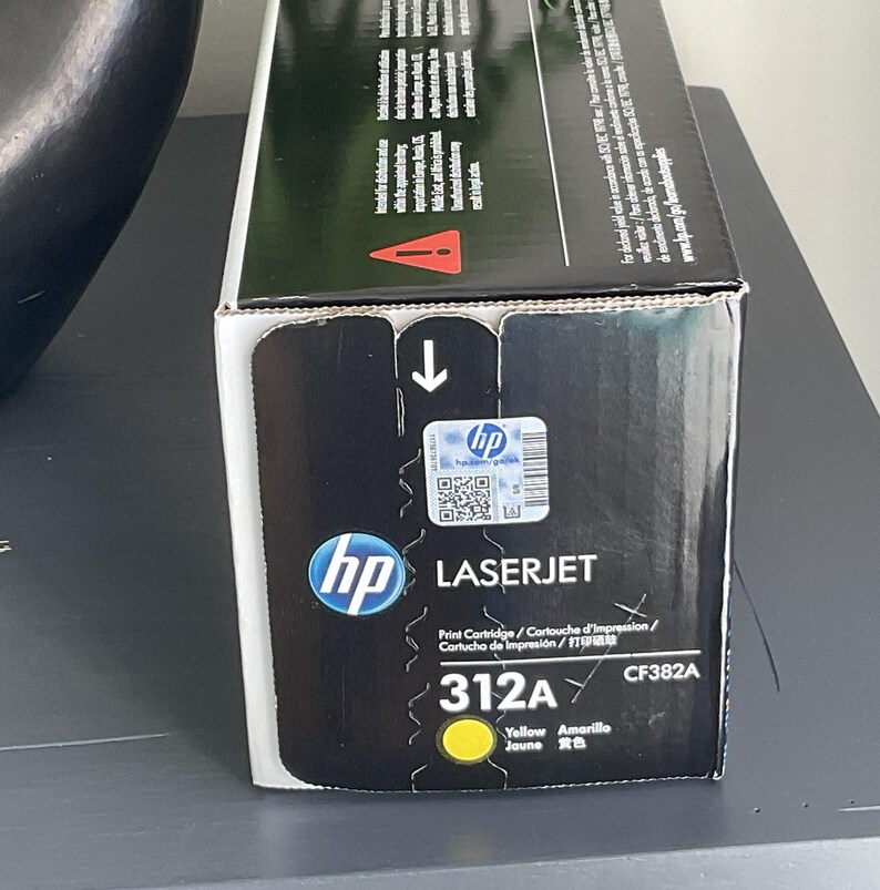 May include: A black and yellow HP LaserJet 312A print cartridge box. The box features the HP logo, product information, and a yellow circle indicating the color. The box also includes the text "Print Cartridge" and "CF382A".