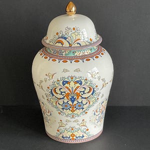 May include: A white ceramic ginger jar with a gold lid and intricate blue, yellow, and orange floral patterns.