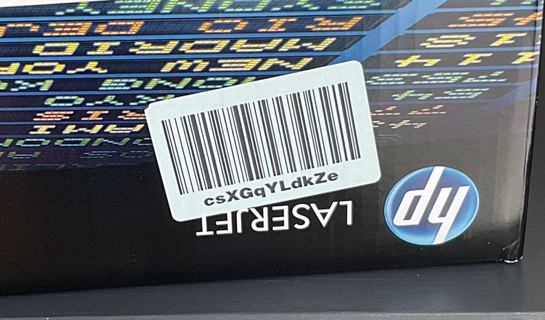 May include: A black HP LaserJet printer box with a white barcode label and the text "csXGgYLdkZe". The HP logo is visible on the lower right corner. The box has a background of city names.