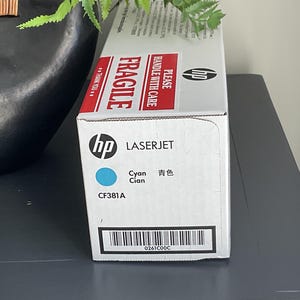 May include: A white HP LaserJet printer cartridge box with red "FRAGILE" and "HANDLE WITH CARE" labels. The box features the HP logo, the word "LASERJET", and "Cyan" in English and Chinese. The model number CF381A is also visible.